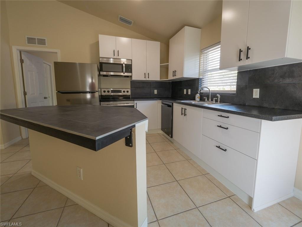 Kitchen with sink, a center island, lofted ceiling, white cabinets, and appliances with stainless steel finishes