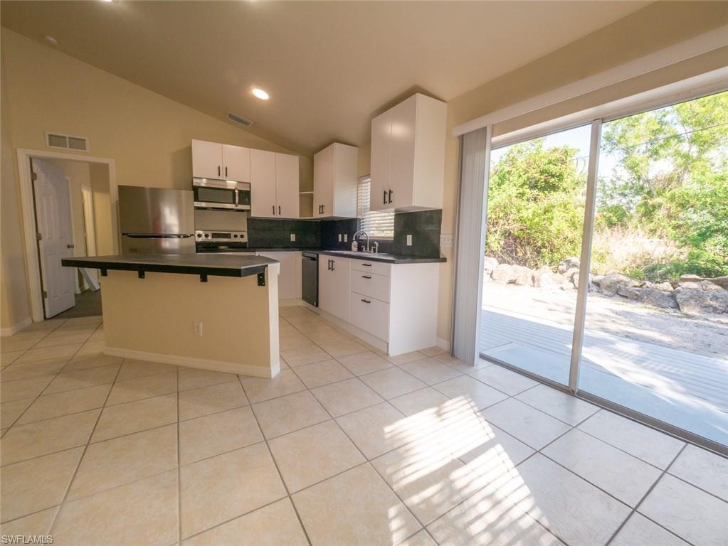 Kitchen featuring vaulted ceiling, light tile patterned floors, appliances with stainless steel finishes, a kitchen island, and white cabinetry