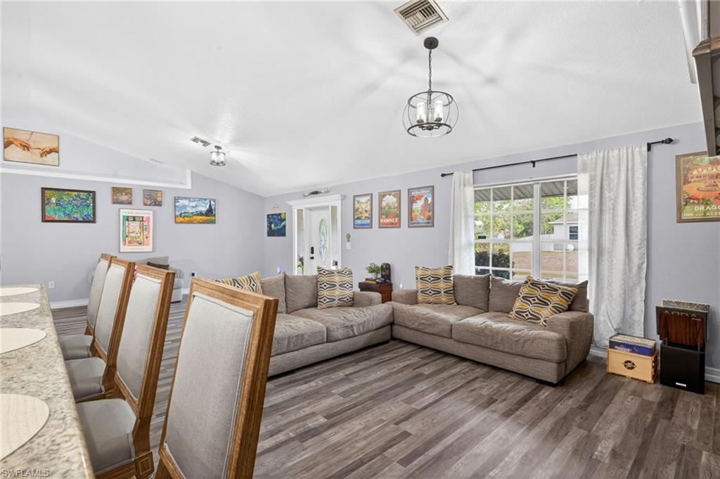 Living room featuring dark wood-style floors, vaulted ceiling, and a chandelier