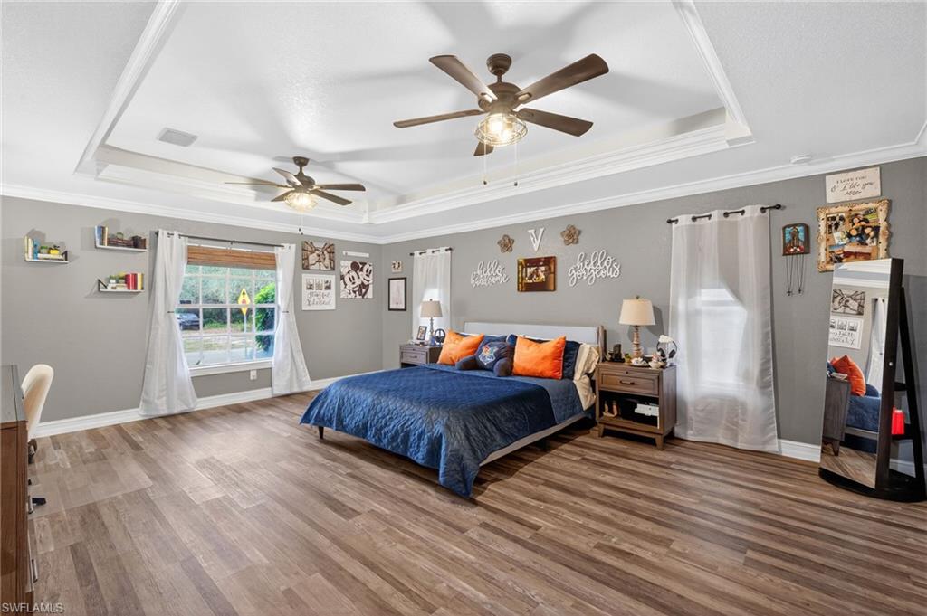 Primary Bedroom with crown molding, wood finished floors, ceiling fan, and a raised ceiling