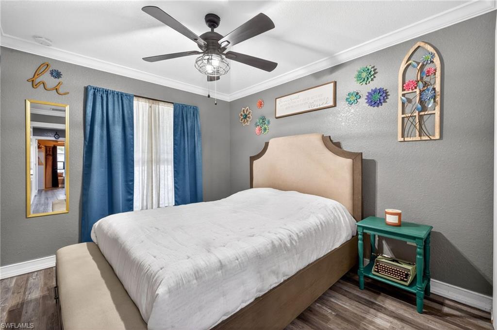 Bedroom featuring a textured wall, wood finished floors, a ceiling fan, and ornamental molding