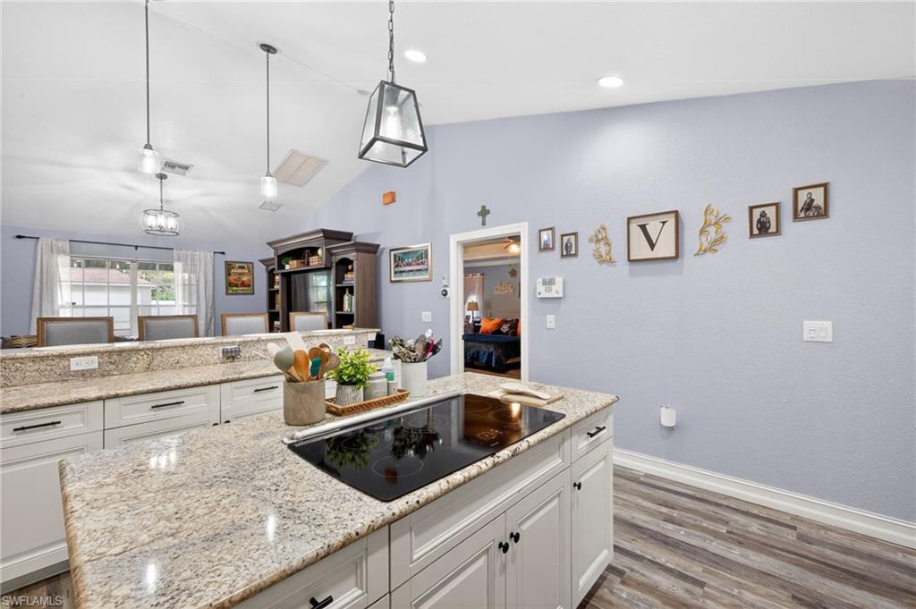 Kitchen with white cabinetry, light stone counters, black electric stovetop, pendant lighting, and a kitchen island
