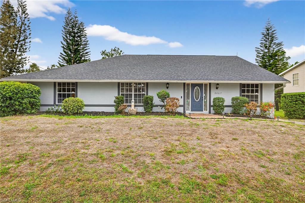 Ranch-style house with stucco siding, roof with shingles, a front lawn, and a porch