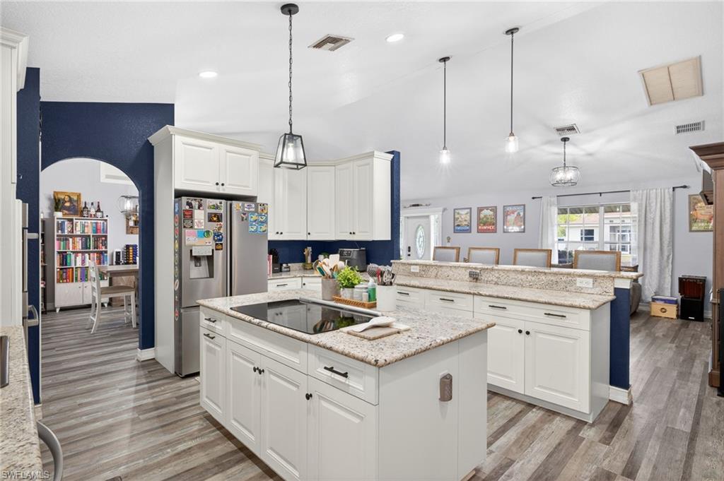 Kitchen with white cabinets, a peninsula, light stone countertops, decorative light fixtures, and vaulted ceiling