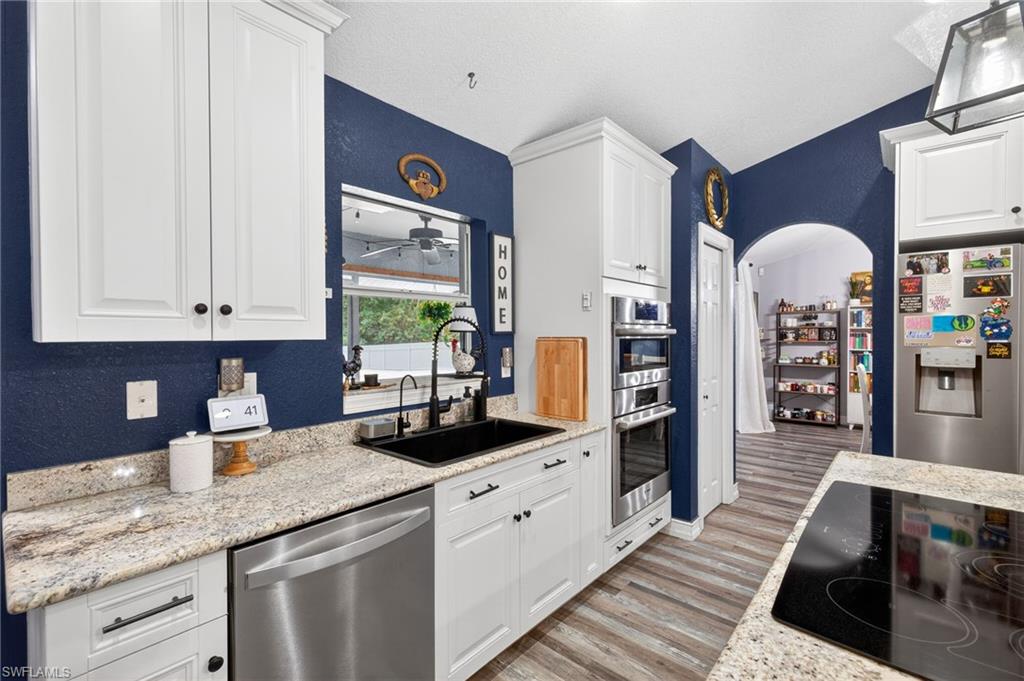 Kitchen with white cabinetry, stainless steel appliances, light wood-style floors, arched walkways, and a textured wall