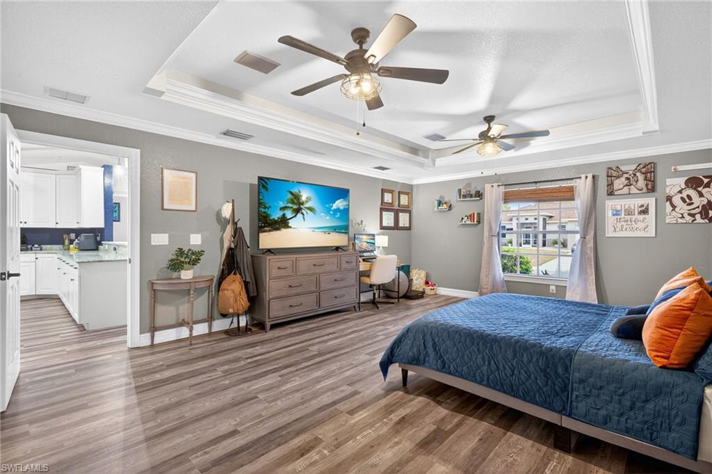 Primary Bedroom featuring crown molding, light wood-type flooring, a raised ceiling, and a ceiling fan