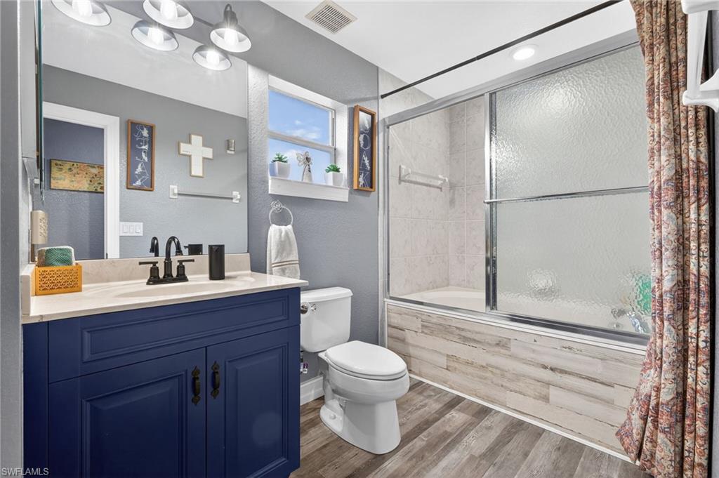 Full bathroom with vanity, a textured wall, combined bath / shower with glass door, and wood finished floors