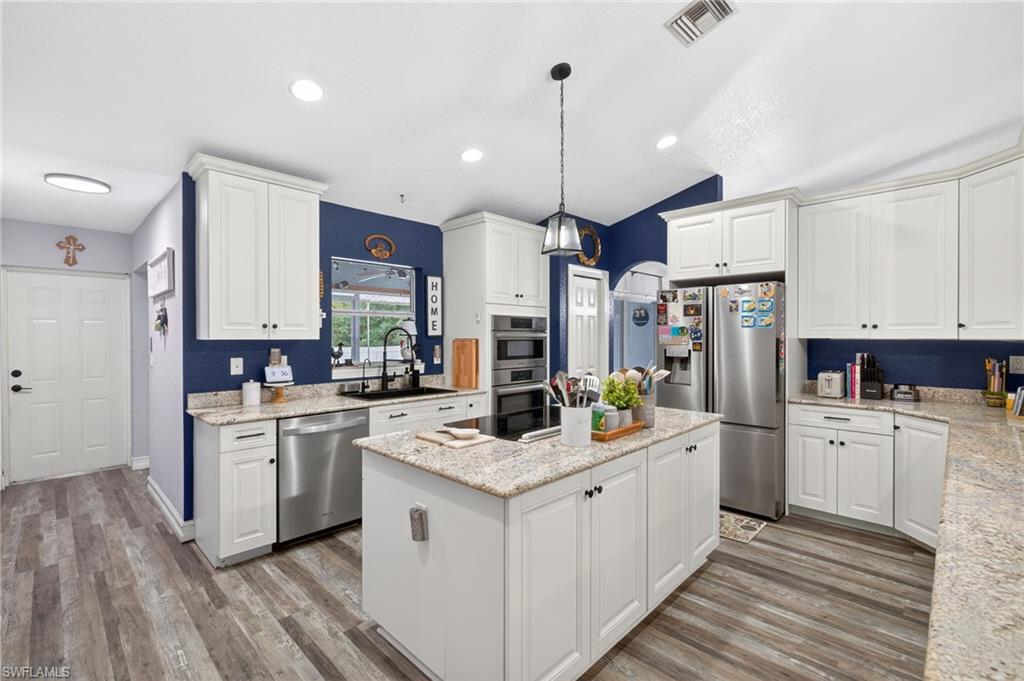 Kitchen with white cabinetry, stainless steel appliances, a kitchen island, light stone countertops, and light wood-type flooring