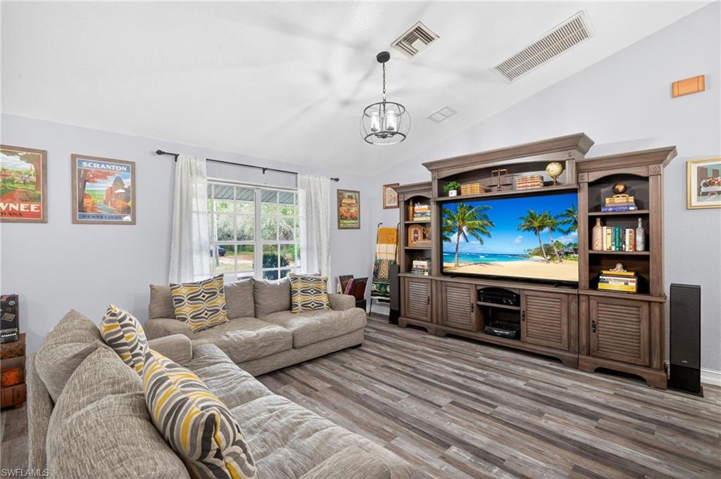 Living room with lofted ceiling, wood finished floors, and suspended lighting