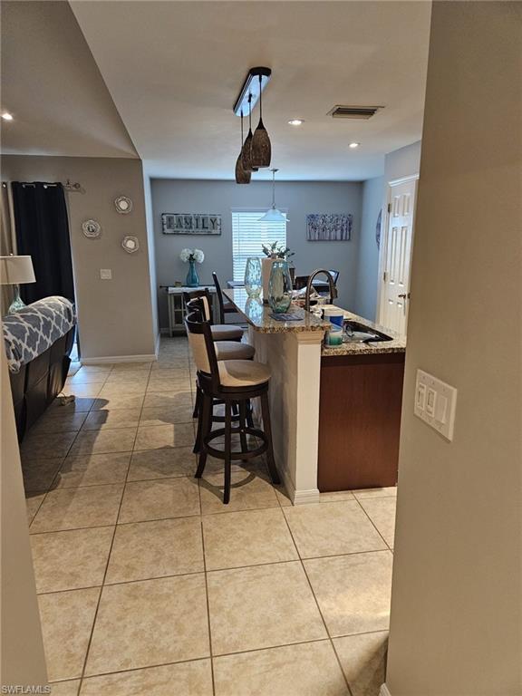 Kitchen with light tile patterned flooring, light stone countertops, an island with sink, a kitchen breakfast bar, and hanging light fixtures