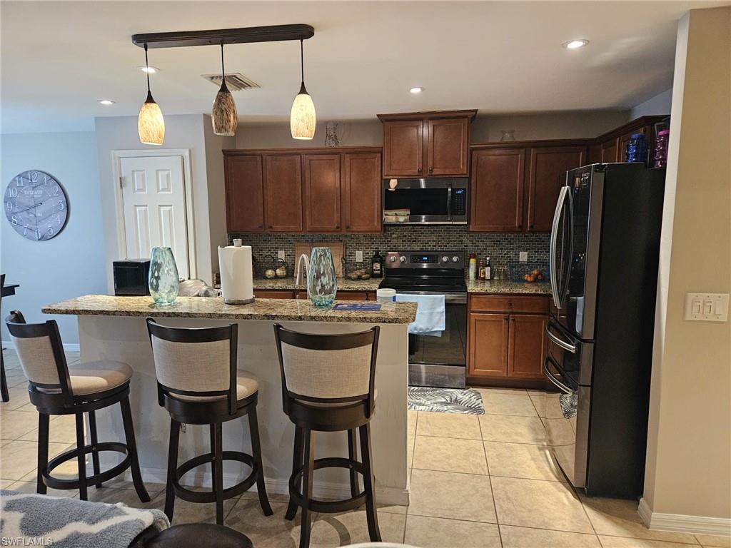 Kitchen featuring stainless steel appliances, a kitchen breakfast bar, a kitchen island with sink, and light tile patterned floors