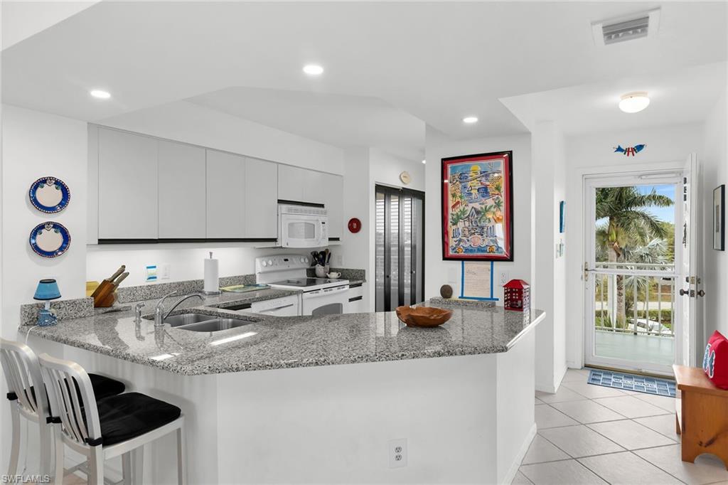 Kitchen with a peninsula, white appliances, light stone countertops, a breakfast bar, and light tile patterned floors