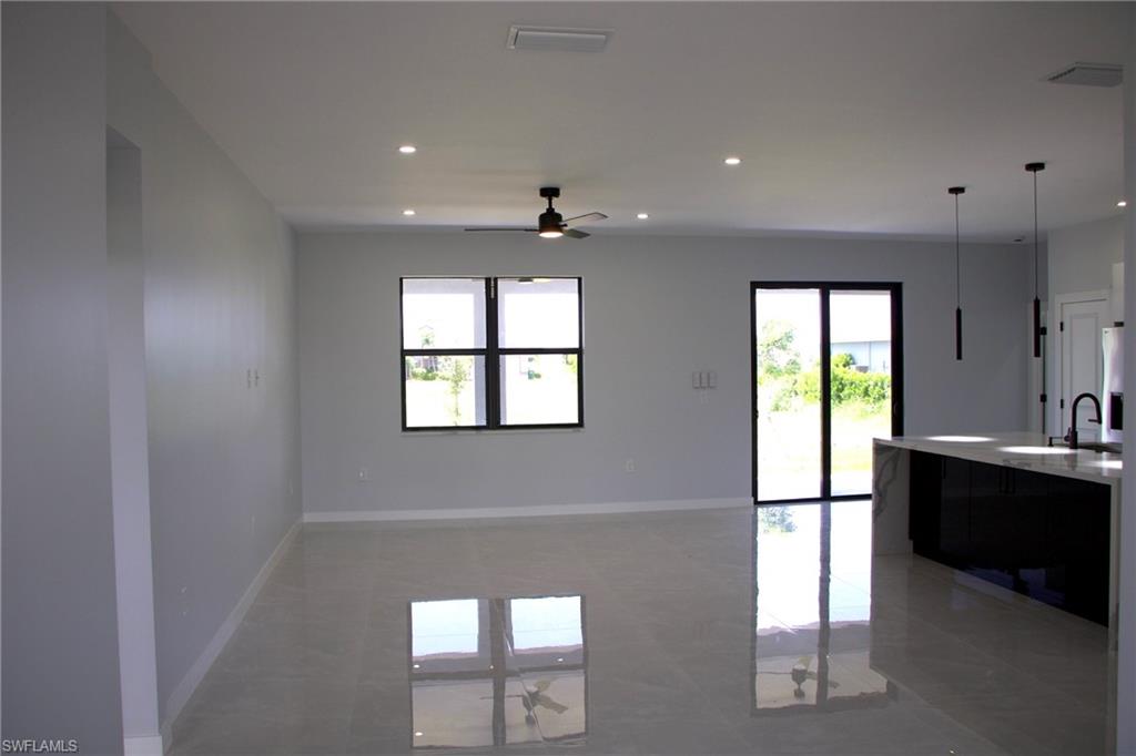 Kitchen featuring a ceiling fan, hanging light fixtures, light stone countertops, open floor plan, and an island with sink