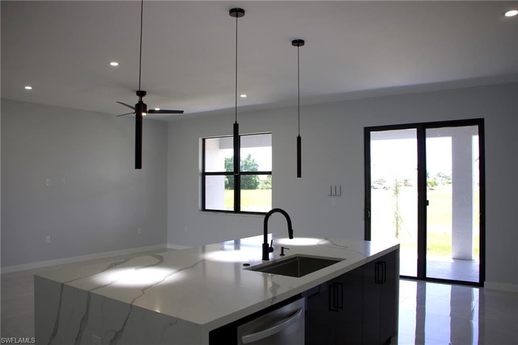 Kitchen with light stone counters, an island with sink, modern cabinets, stainless steel dishwasher, and a ceiling fan