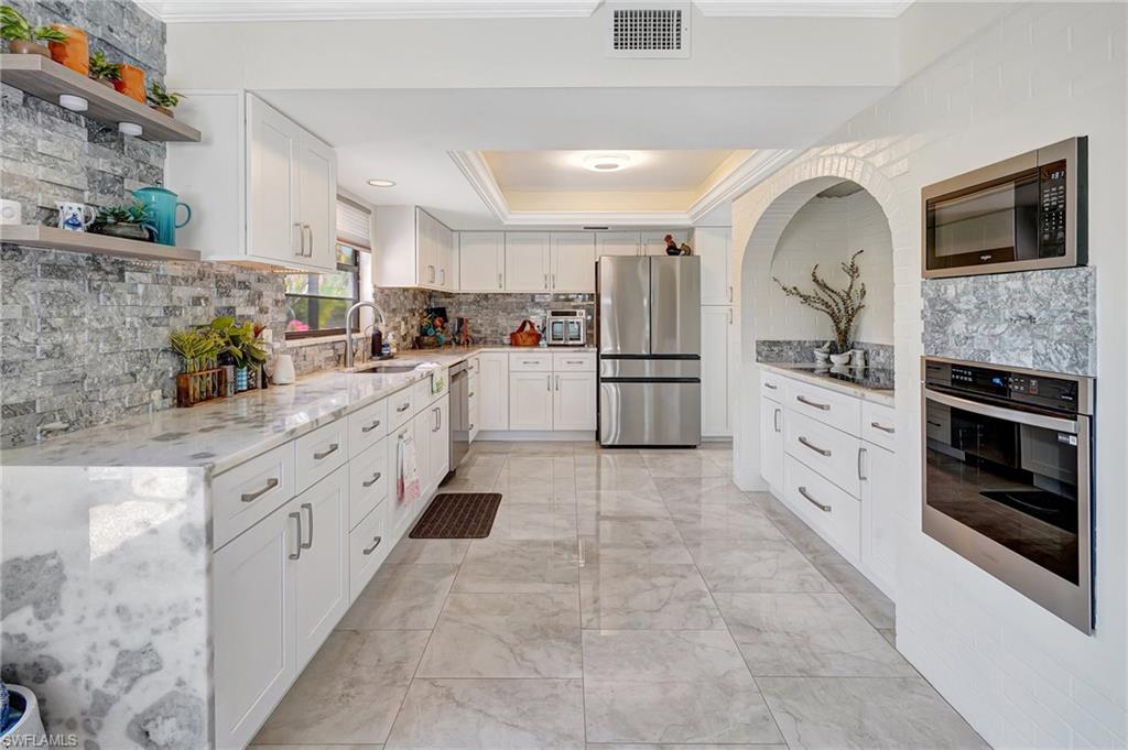 Kitchen with, appliances with stainless steel finishes, a sink, open shelves, and a tray ceiling