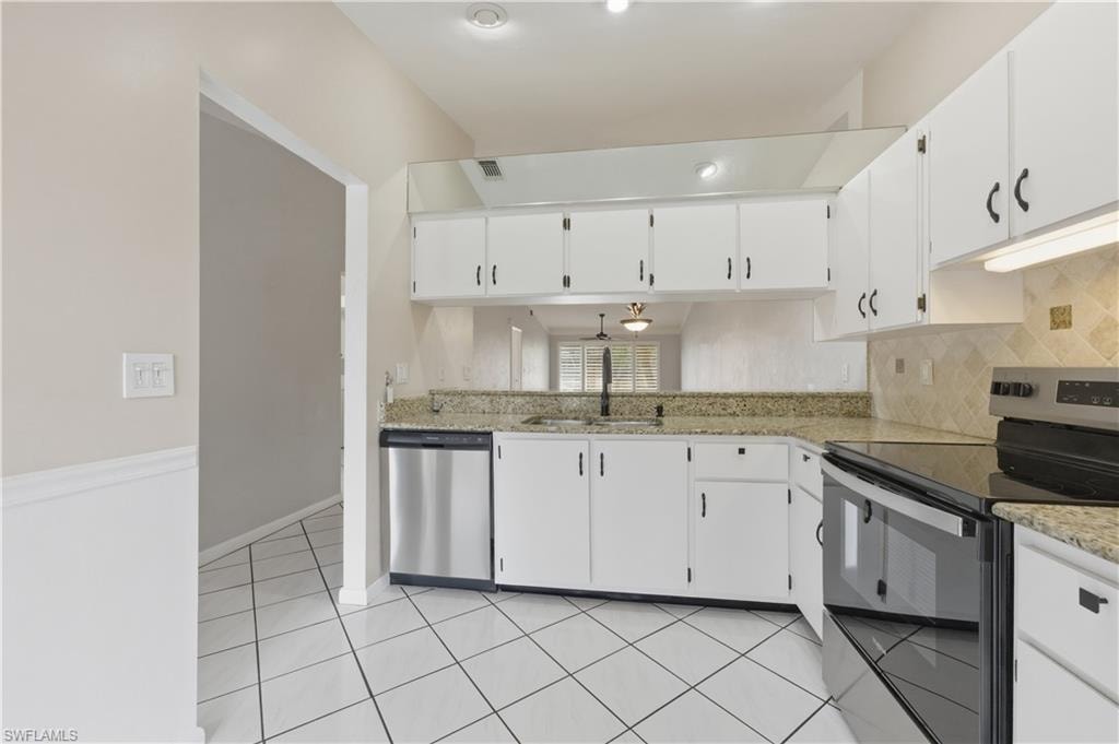 Kitchen featuring stainless steel appliances, white cabinetry, light stone countertops, and tasteful backsplash