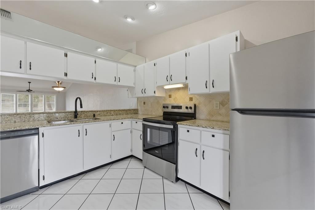Kitchen featuring stainless steel appliances, white cabinets, light stone counters, and tasteful backsplash