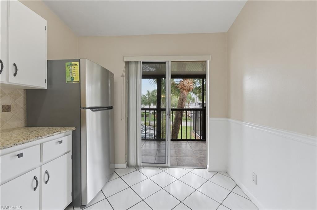 Kitchen featuring white cabinetry, freestanding refrigerator, light tile patterned floors, and backsplash