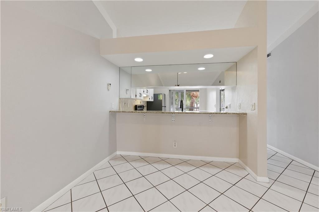 Kitchen with light stone countertops, white cabinetry, a peninsula, freestanding refrigerator, and recessed lighting