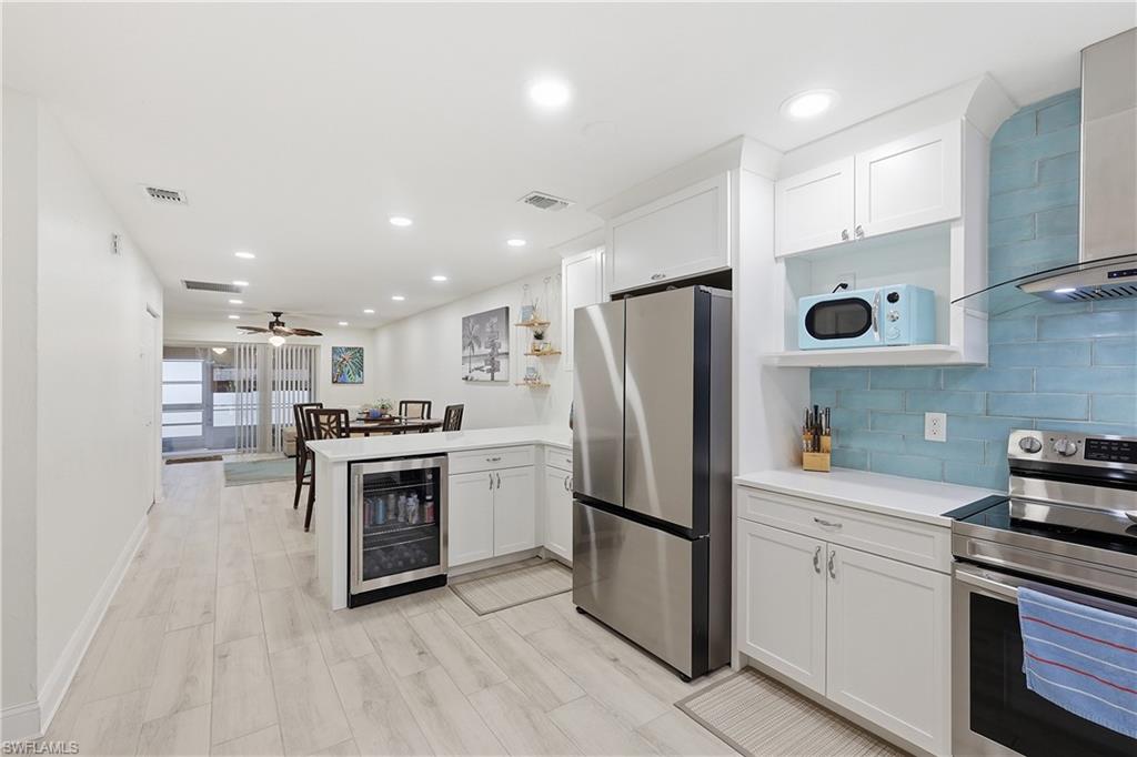 Kitchen with stainless steel appliances, a peninsula, beverage cooler, white cabinets, and recessed lighting