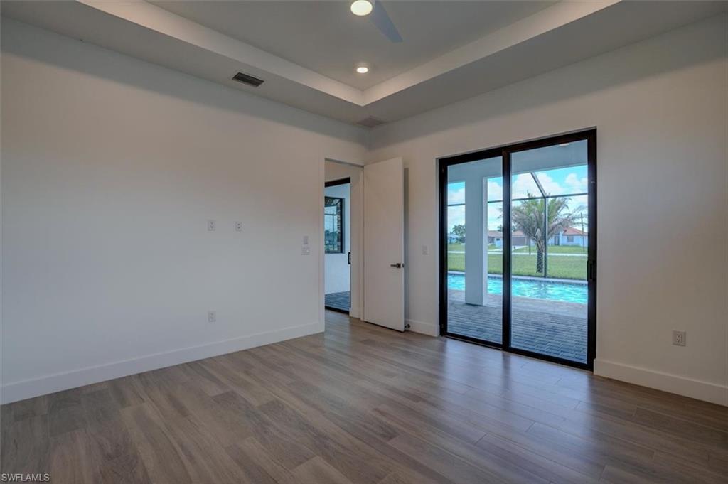 Empty room with ceiling fan, a tray ceiling, and wood-type flooring