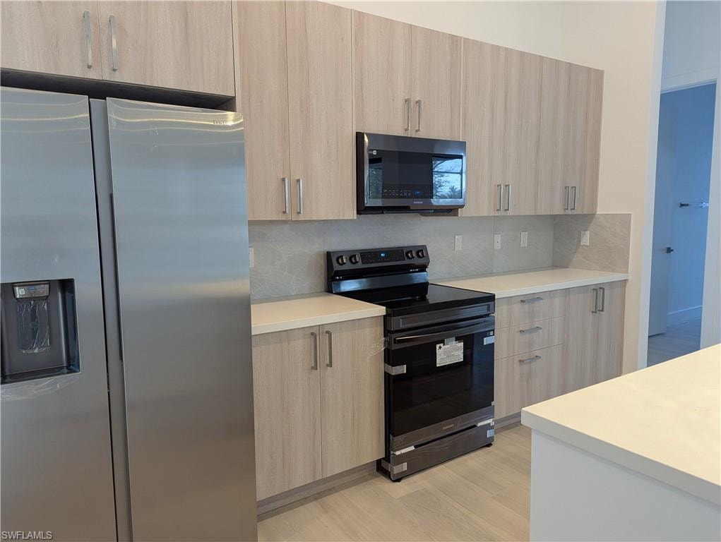 Kitchen featuring stainless steel fridge with ice dispenser, light brown cabinetry, and black electric range