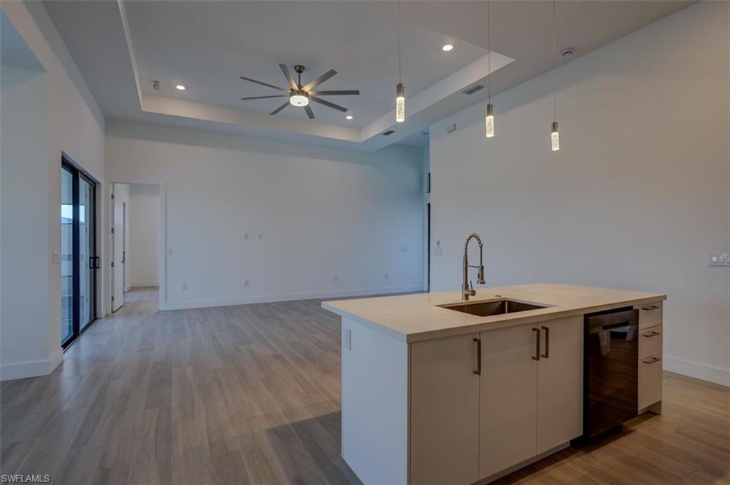 Kitchen featuring ceiling fan, a tray ceiling, sink, light hardwood / wood-style floors, and a kitchen island with sink