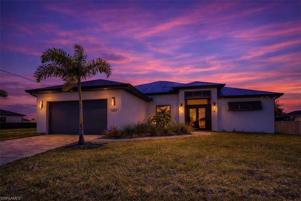 View of front of property featuring a front lawn, a garage, driveway, stucco siding, and french doors