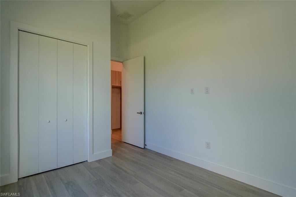 Unfurnished bedroom with light hardwood / wood-style floors, a closet, and a high ceiling