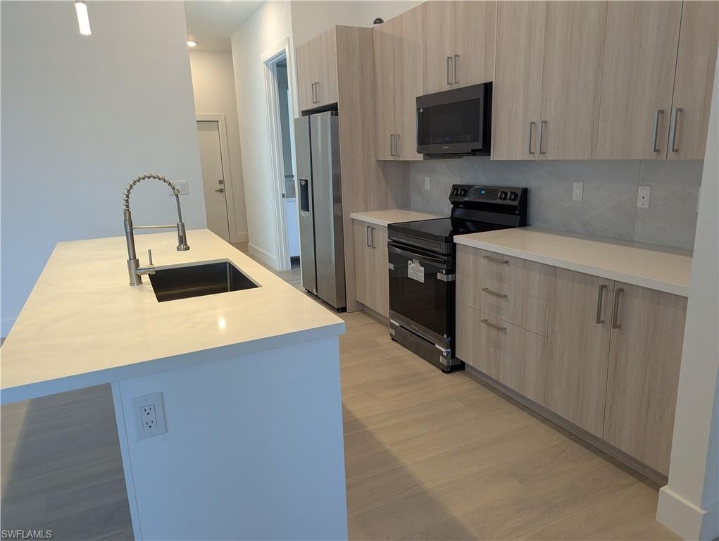 Kitchen featuring stainless steel refrigerator with ice dispenser, black range with electric cooktop, sink, light brown cabinets, and an island with sink
