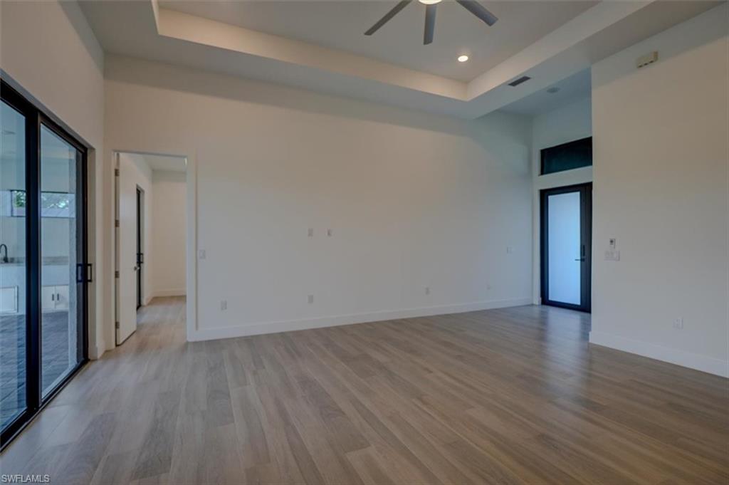 Empty room featuring light hardwood / wood-style floors, ceiling fan, a raised ceiling, and a high ceiling
