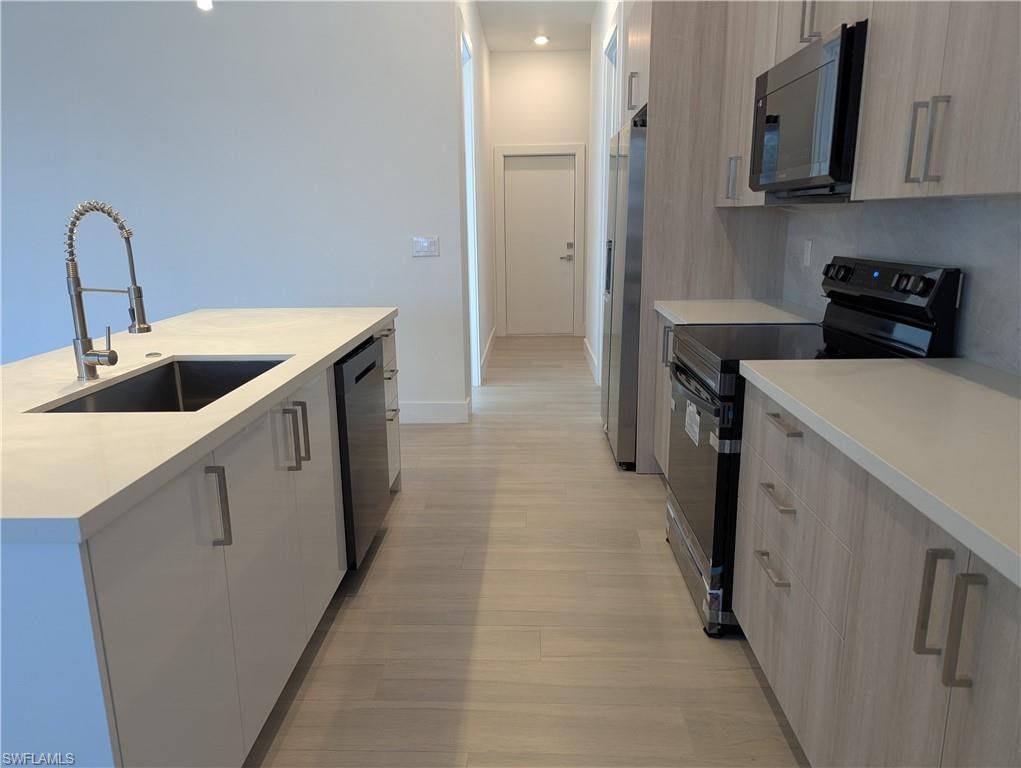 Kitchen featuring light brown cabinets, sink, light wood-type flooring, an island with sink, and appliances with stainless steel finishes