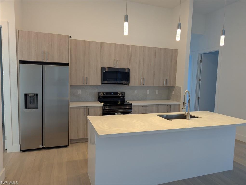 Kitchen featuring appliances with stainless steel finishes, light brown cabinetry, tasteful backsplash, sink, and a center island with sink