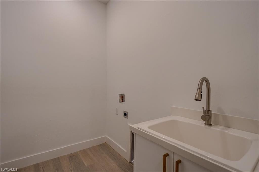 Laundry area with hookup for a washing machine, light hardwood / wood-style floors, electric dryer hookup, and sink