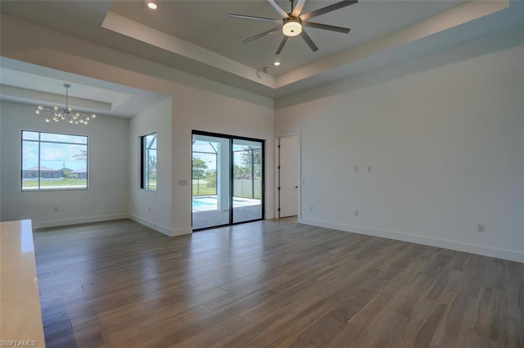 Empty room with ceiling fan with notable chandelier, a high ceiling, hardwood / wood-style floors, and a tray ceiling