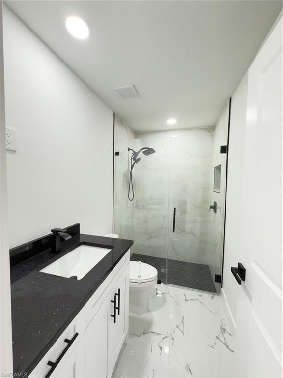 Bathroom featuring vanity, a marble finish shower, and recessed lighting