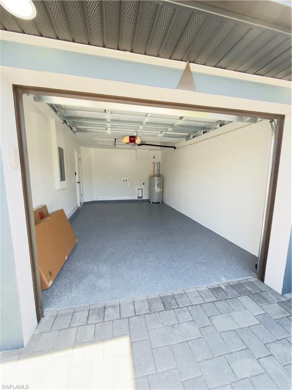 Garage with electric water heater, electric panel, and a garage door opener