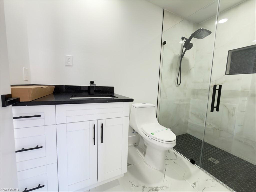 Bathroom featuring vanity, a marble finish shower, and light marble finish floors