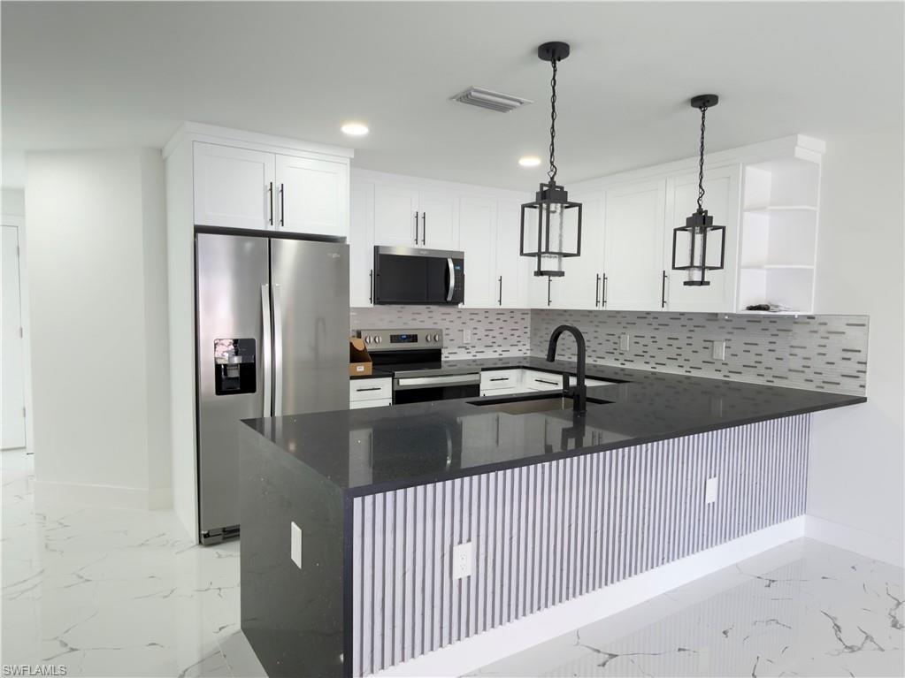Kitchen with dark stone counters, a peninsula, stainless steel appliances, light marble finish flooring, and open shelves