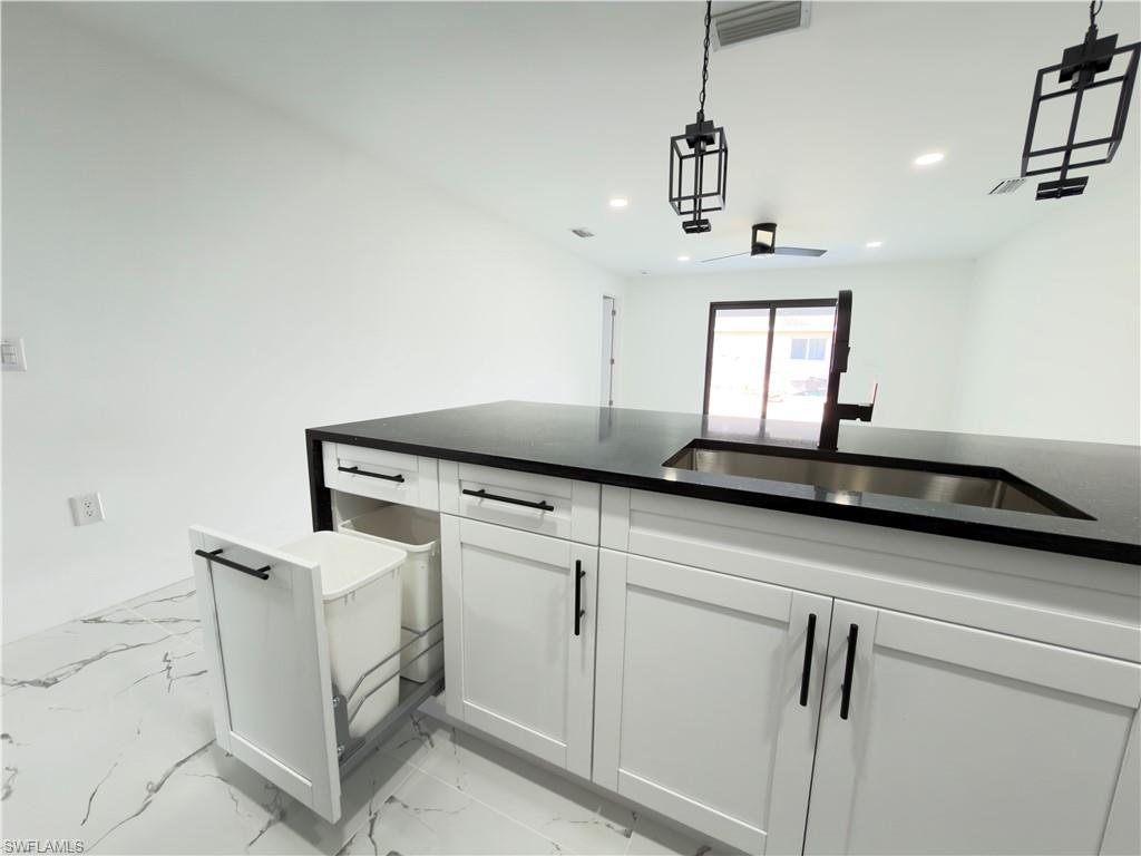 Kitchen with dark stone countertops, white cabinetry, decorative light fixtures, and light marble finish floors