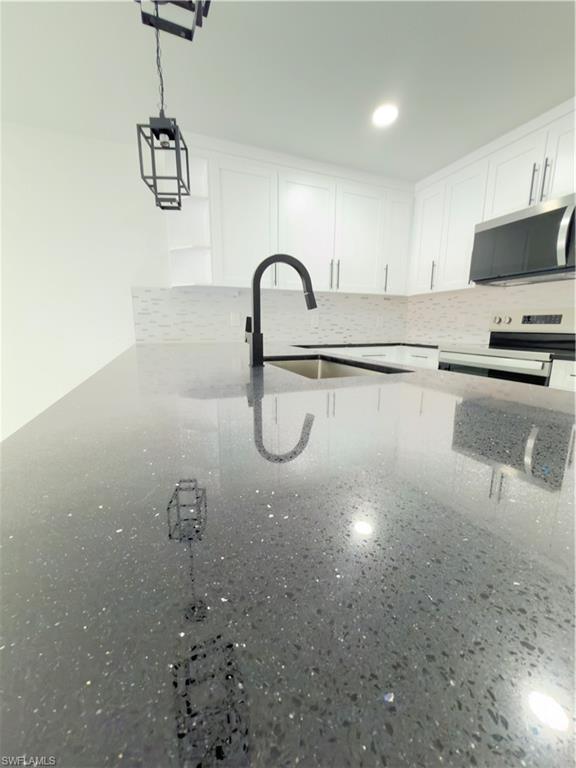 Kitchen view of white cabinets, light stone counters, range, and decorative backsplash