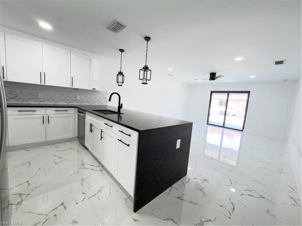 Kitchen featuring a peninsula, dark stone countertops, decorative light fixtures, white cabinets, and light marble finish flooring