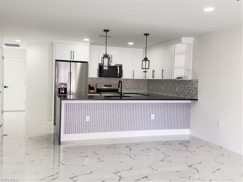 Kitchen with dark stone counters, a peninsula, open shelves, white cabinets, and range