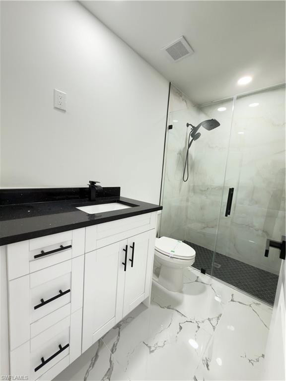 Bathroom featuring vanity, a marble finish shower, light marble finish floors, and recessed lighting