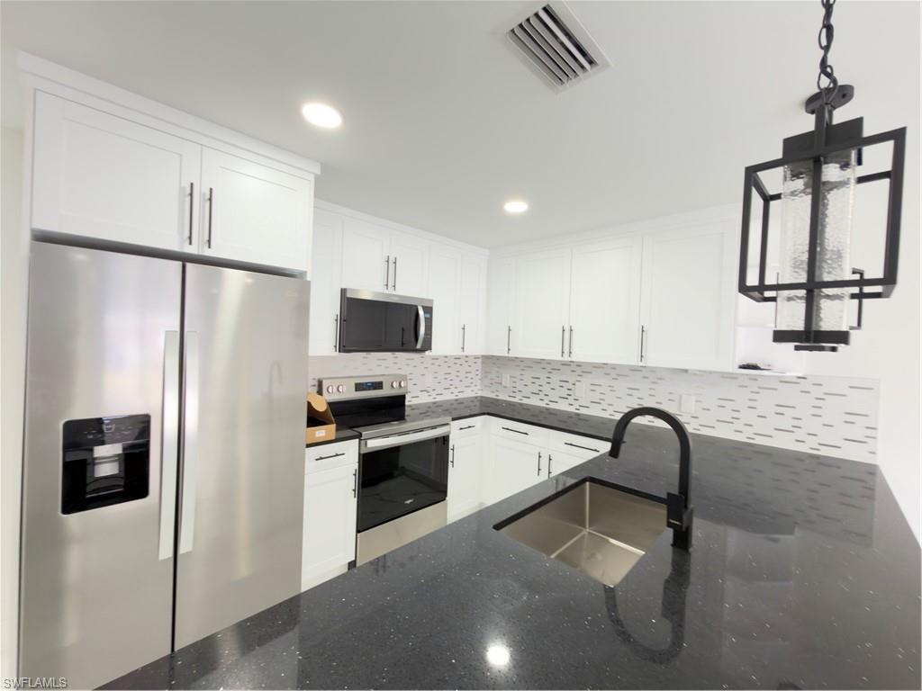 Kitchen featuring refrigerator, white cabinetry, range, and hanging light fixtures