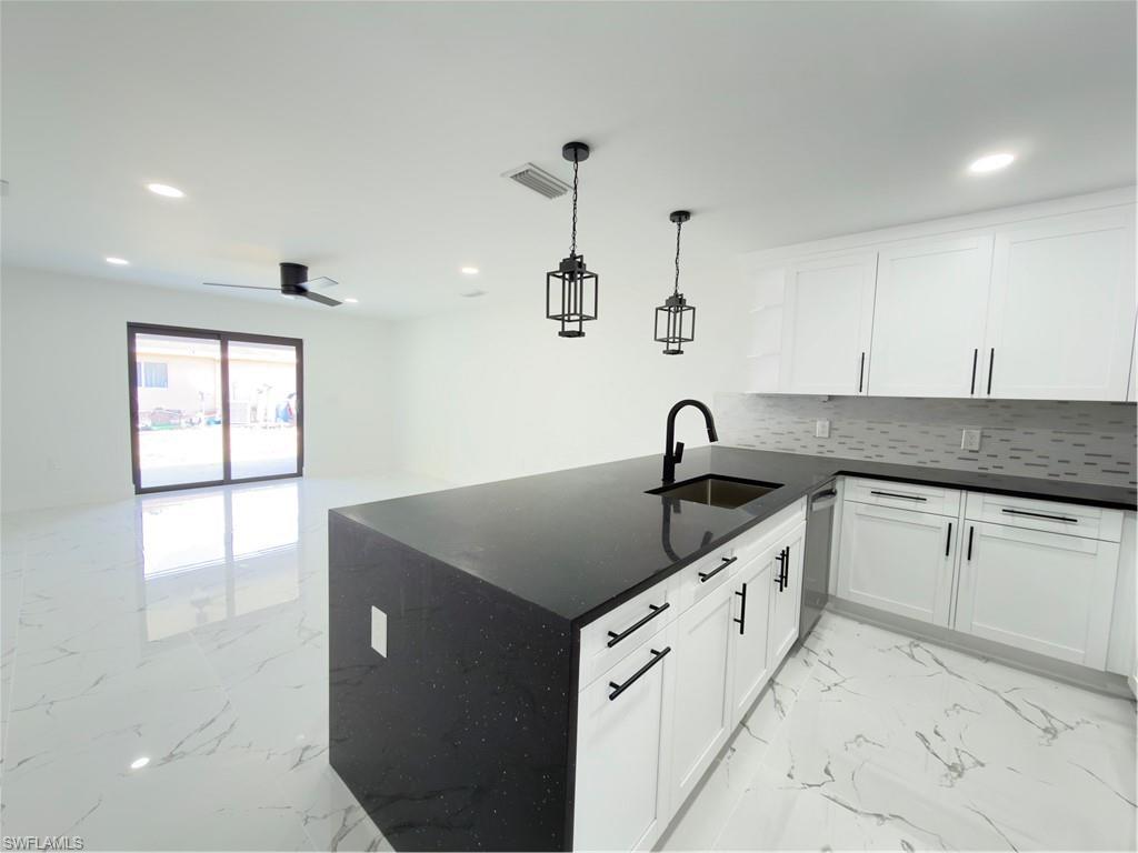 Kitchen featuring open shelves, light marble finish floors, dark stone countertops, a peninsula, and white cabinetry