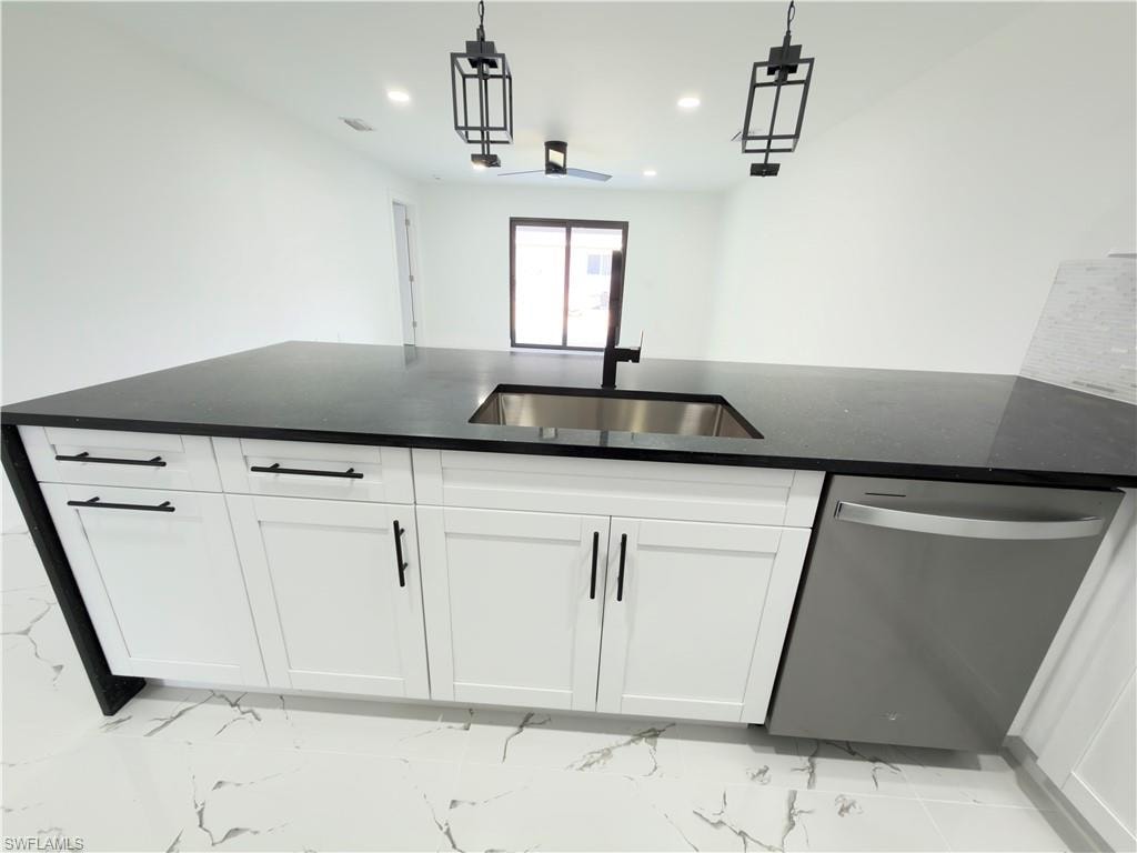 Kitchen featuring stainless steel dishwasher, white cabinets, dark stone counters, and hanging light fixtures