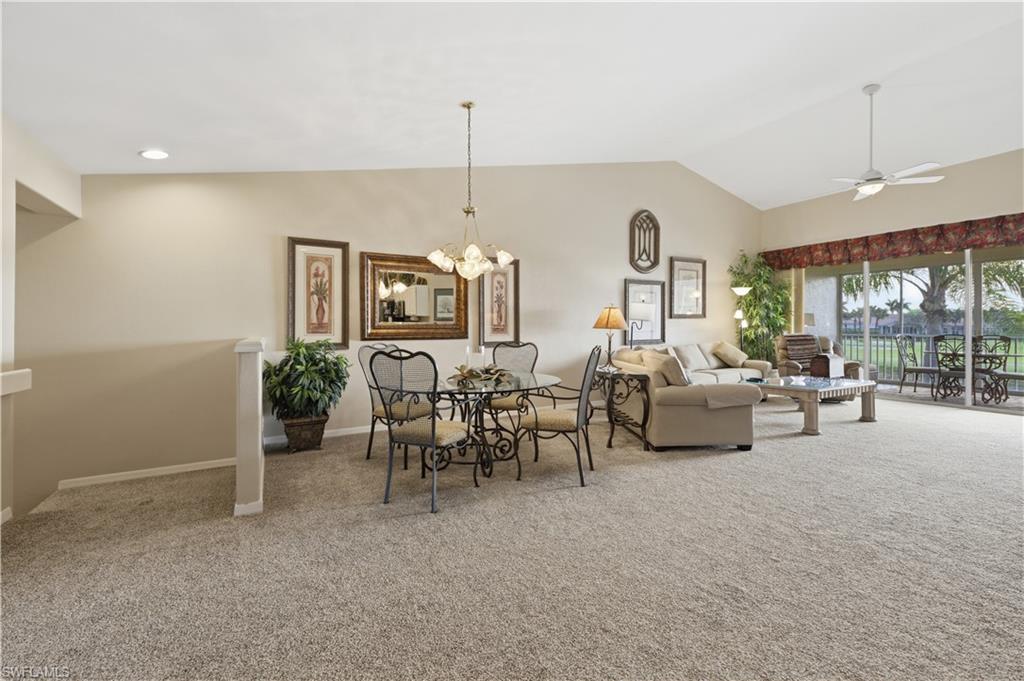 Living area with a ceiling fan, light colored carpet, hanging lights, and lofted ceiling