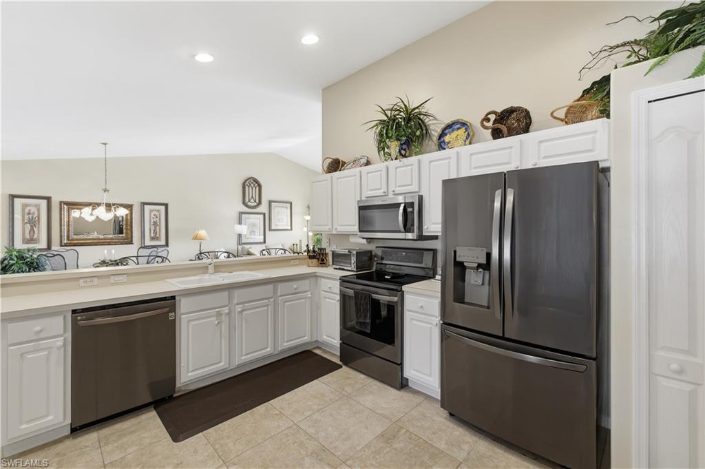 Kitchen with stainless steel appliances, light countertops, white cabinetry, lofted ceiling, and light tile patterned floors