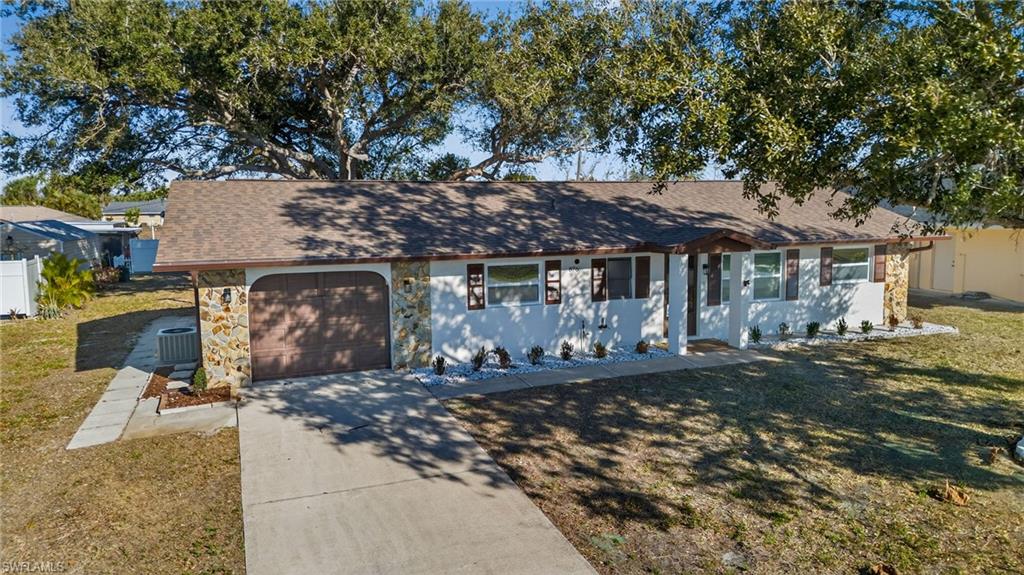 Single story home featuring a shingled roof, an attached garage, driveway, a front yard, and stone siding